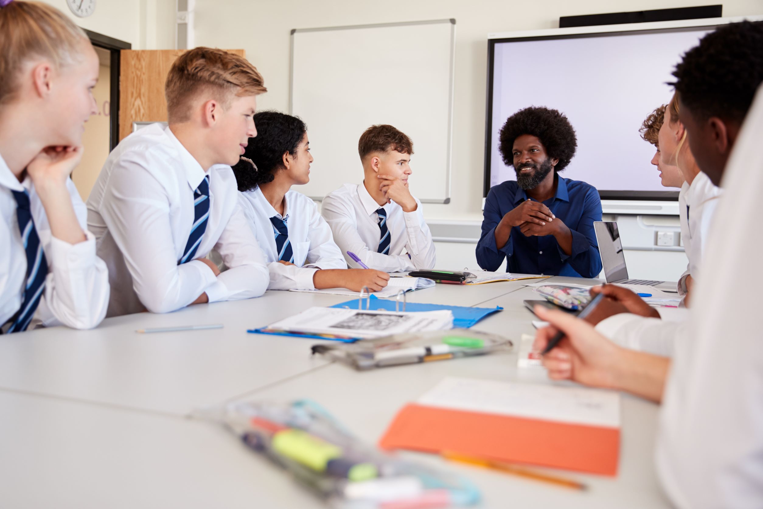 male teacher at a table with secondary school students